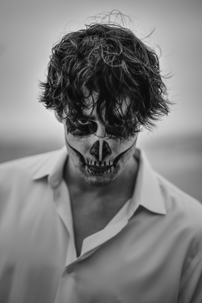 Moody black and white portrait of an adult with skull face paint, evoking a Halloween theme.