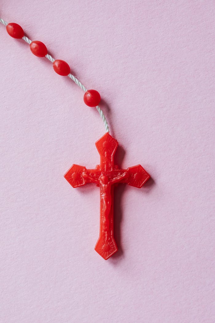 A red rosary laid on a pastel pink surface symbolizing faith and spirituality.